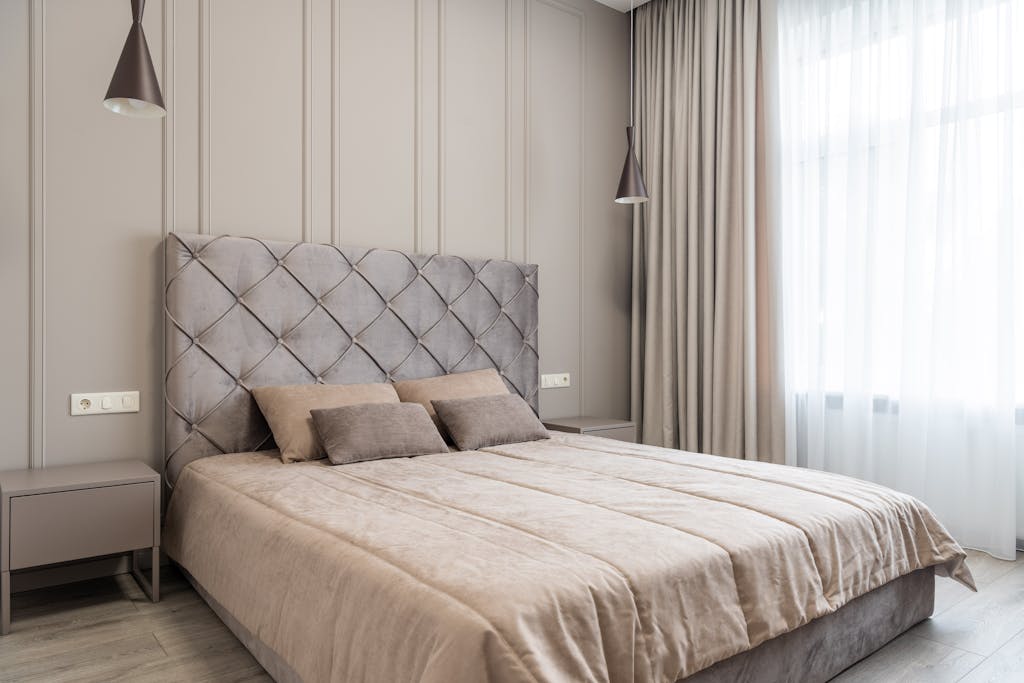 Interior of modern light bedroom with pillows on bed near tables under lamps and windows with curtains