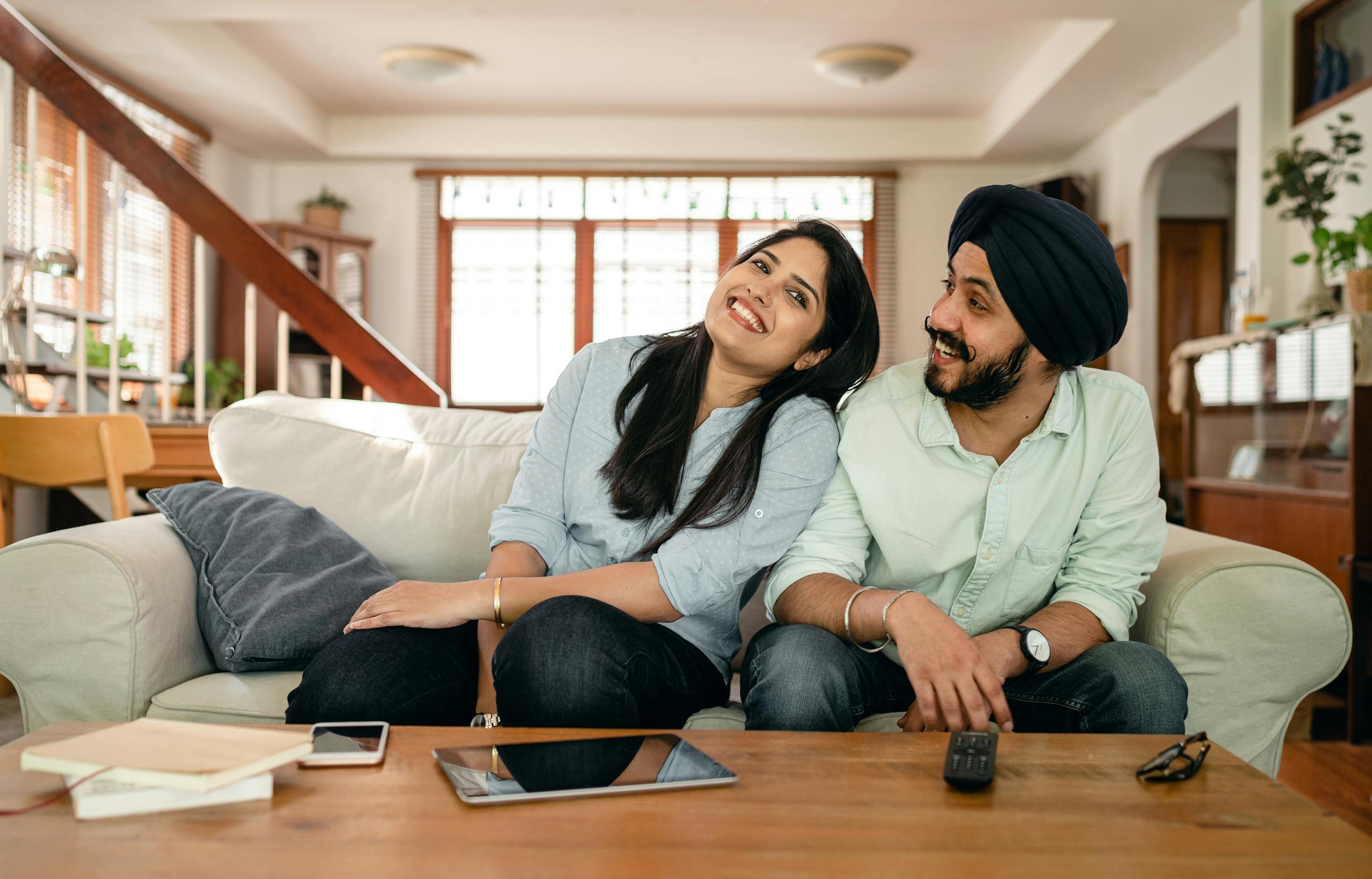 Optimistic young Indian lady in casual wear flirting with happy boyfriend while chilling on comfortable couch